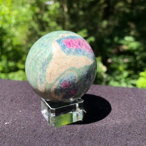 May include: A green, blue, and pink sphere of polished ruby zoisite on a clear glass stand.