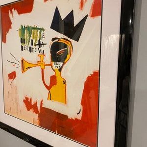 May include: Framed art print depicting an abstract figure with a crown and trumpet. The artwork features a yellow torso, black face, and a red and white background. The black frame provides a contemporary aesthetic.