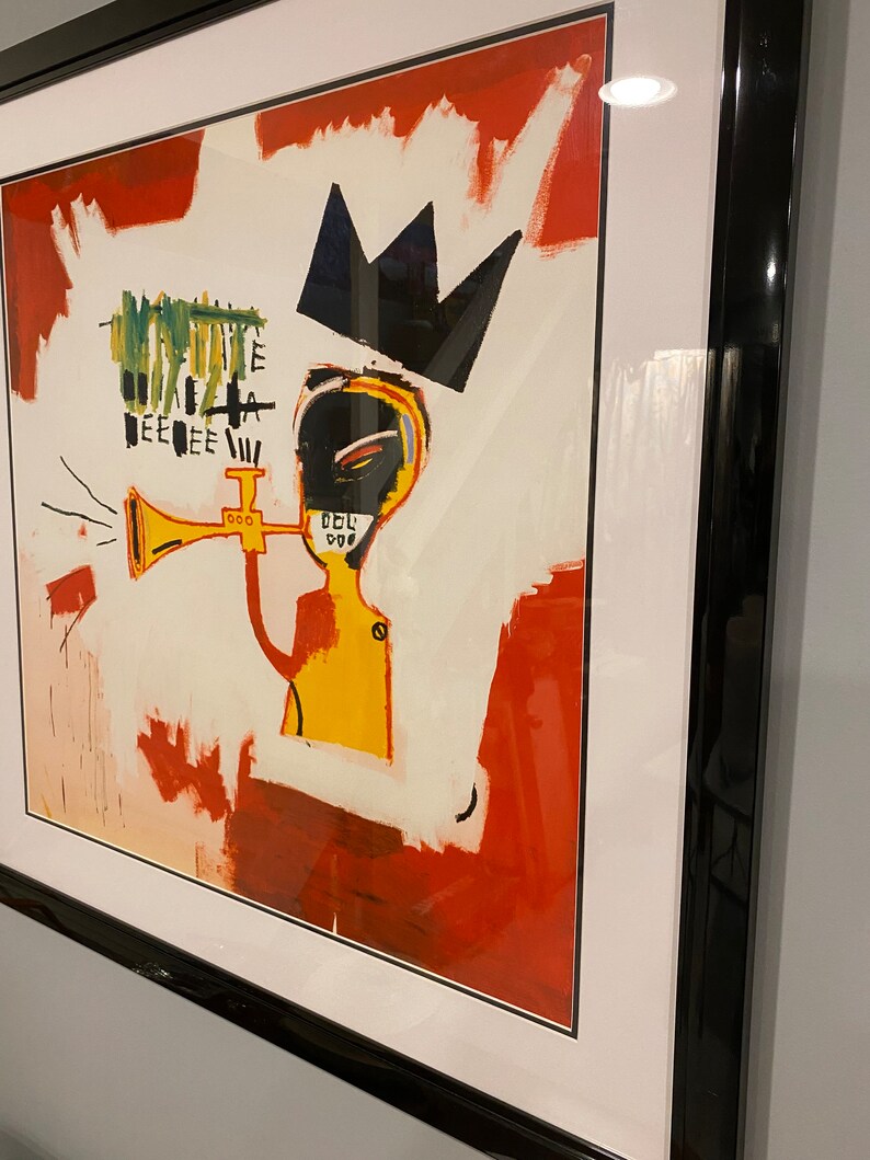 May include: Framed art print depicting an abstract figure with a crown and trumpet. The artwork features a yellow torso, black face, and a red and white background. The black frame provides a contemporary aesthetic.
