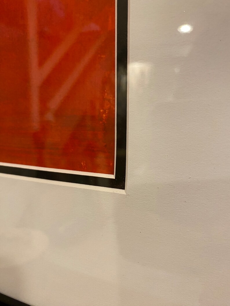 May include: Framed artwork with a vivid red background and white, abstract lines. The artwork is enclosed in a black frame with a white border, creating a striking contrast. The piece is mounted on a white wall.