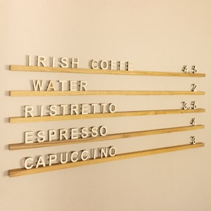 May include: A wooden sign with a list of coffee drinks and their prices. The drinks listed are Irish Coffee, Water, Ristretto, Espresso, and Cappuccino. The prices are 4.5, 2, 3.5, 4, and 3.