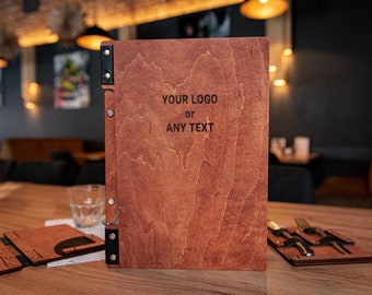 May include: A wooden menu cover with a dark brown finish. The cover has a black leather strap and metal rivets. The text "YOUR LOGO or ANY TEXT" is engraved on the front.