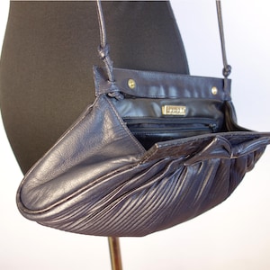 May include: A dark navy blue leather crossbody bag with a pleated design. The bag has a flap closure and a long strap. The interior is visible, revealing a zippered pocket and a label that reads "SPORTE".