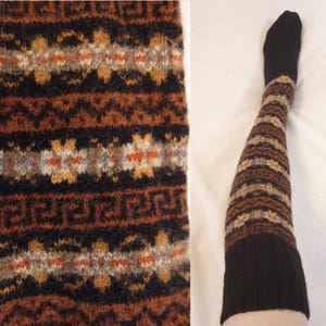 May include: A pair of over-the-knee socks featuring a black toe and a wide black cuff at the top. The leg portion displays a repeating knit pattern in shades of brown, tan, orange, and black, including geometric shapes and star-like motifs.