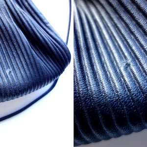 May include: Close-up of a navy blue, pleated handbag. The bag has a textured, ridged surface and a thin, matching strap. The image highlights the bag's design and material, showcasing its unique texture and color.