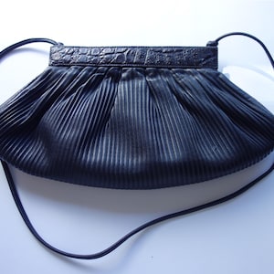 May include: Black pleated handbag with a long strap. The top of the bag has a textured, crocodile-like design. The bag's body is made of a pleated material, creating a textured effect. The strap is thin and appears to be made of the same material as the bag.
