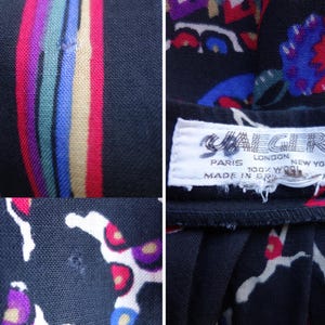 May include: A black wool garment featuring a multi-coloured floral and striped pattern. A white fabric label is stitched to the interior, displaying the text JAEGER, PARIS LONDON NEW YORK, 100% WOOL, MADE IN GREAT BRITAIN. Small holes are visible in the fabric.