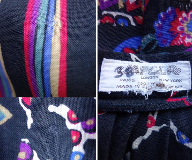 May include: A black wool garment featuring a multi-coloured floral and striped pattern. A white fabric label is stitched to the interior, displaying the text JAEGER, PARIS LONDON NEW YORK, 100% WOOL, MADE IN GREAT BRITAIN. Small holes are visible in the fabric.