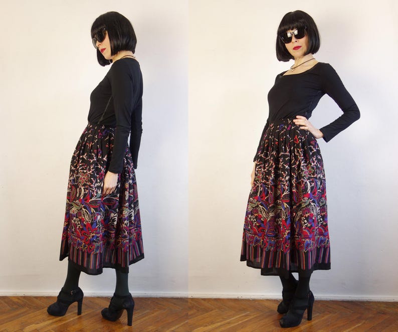 May include: A long-sleeved black top paired with a mid-calf length skirt featuring a vibrant, multi-coloured floral and abstract pattern on a black background, finished with a vertical striped border at the hemline and a gathered, full silhouette.