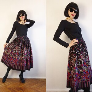 May include: A long-sleeved black top paired with a high-waisted, pleated midi skirt featuring a vibrant, multi-coloured floral and paisley pattern on a black background, finished with a striped border at the hemline.