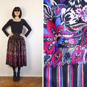 May include: A midi-length skirt featuring a black base with a vibrant floral and paisley pattern in shades of magenta, blue, purple, and cream. The skirt has a gathered waistline and a hem decorated with a repeating leaf motif and vertical stripes.