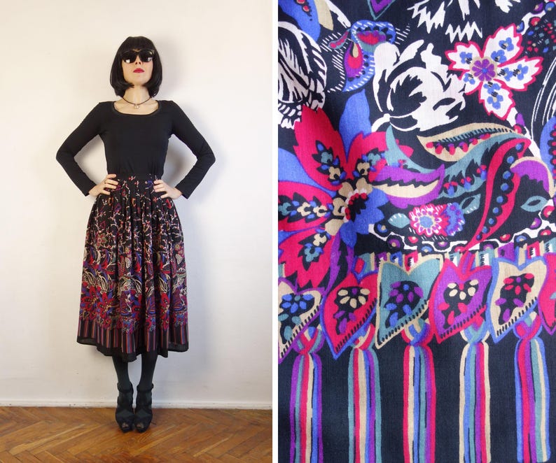 May include: A midi-length skirt featuring a black base with a vibrant floral and paisley pattern in shades of magenta, blue, purple, and cream. The skirt has a gathered waistline and a hem decorated with a repeating leaf motif and vertical stripes.