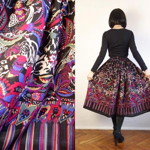 May include: A black midi skirt featuring a vibrant, multicoloured floral and paisley print with butterflies. The skirt has a gathered waist and a wide, striped border at the hem. The fabric is lightweight and pleated, creating a full, flared silhouette.