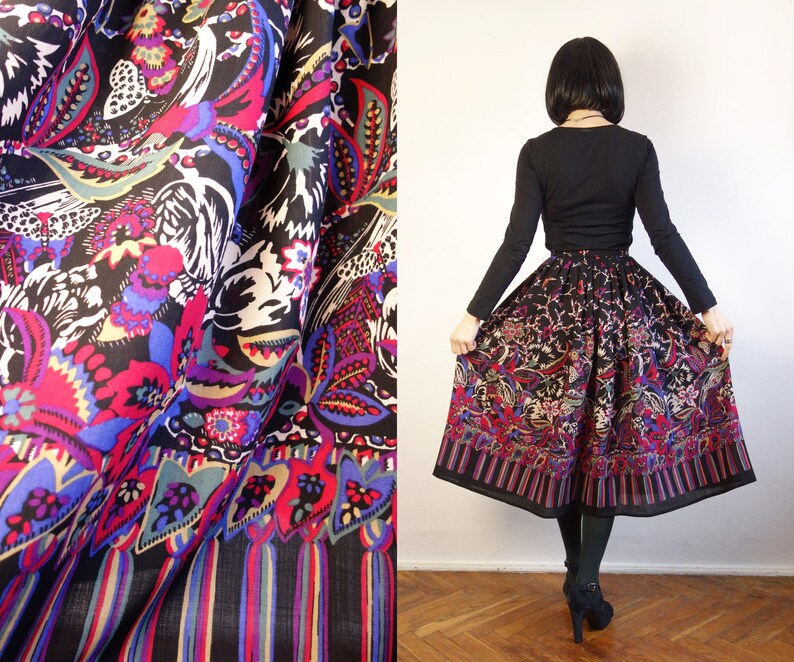 May include: A black midi skirt featuring a vibrant, multicoloured floral and paisley print with butterflies. The skirt has a gathered waist and a wide, striped border at the hem. The fabric is lightweight and pleated, creating a full, flared silhouette.