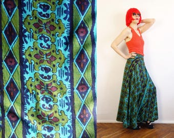 May include: A floor-length wrap skirt featuring a vibrant pattern of teal, olive green, and dark purple geometric shapes and floral motifs. The skirt is paired with a sleeveless orange ribbed top, creating a colourful ensemble with a flowing silhouette.