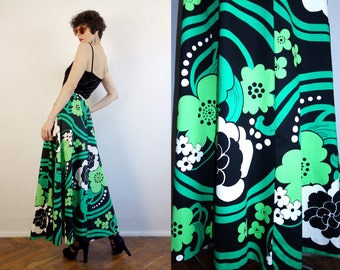 May include: A floor-length skirt featuring a bold graphic pattern of large black, white, and bright green flowers with wavy lines and dots. The skirt is paired with a black sleeveless top with thin spaghetti straps and a velvet-like texture.