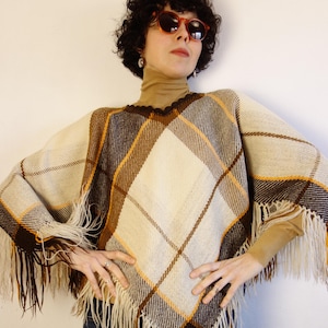 May include: A vintage poncho in a plaid pattern with cream, brown, and yellow hues. The poncho has a fringed hem and a V-neck design. The garment is made of a woven fabric, offering a retro aesthetic.