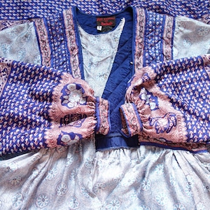 May include: A vintage blue and pink patterned dress with long sleeves. The dress features a quilted bodice and a floral print on the sleeves and skirt. The fabric has a soft, flowing appearance, suggesting a comfortable fit.