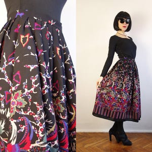May include: A black midi skirt featuring a vibrant, multi-coloured floral and abstract pattern with shades of red, purple, blue, and white. The skirt has a high-waisted design with structured pleats that create a full, flared silhouette.