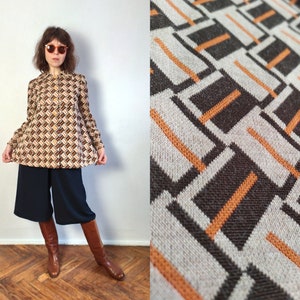 Puede incluir: Una blusa de estilo vintage con un patrón geométrico en tonos marrón, beige y naranja. Se combina con unos pantalones culotte azul marino y botas altas marrones. La tela tiene una apariencia texturizada y el estilo general es retro.