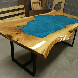 Puede incluir: Una mesa de madera grande con un borde vivo y una incrustaci&oacute;n de resina epoxi azul turquesa. La mesa tiene una base de metal negro.