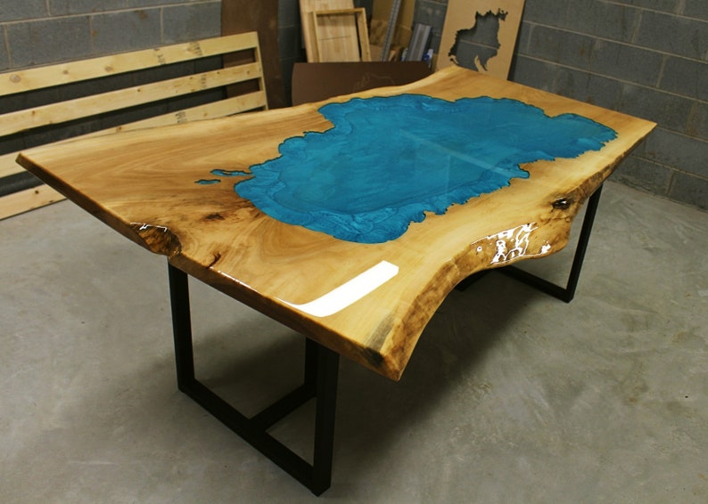 Puede incluir: Una mesa de madera grande con un borde vivo y una incrustaci&oacute;n de resina epoxi azul turquesa. La mesa tiene una base de metal negro.