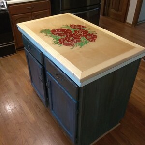 Puede incluir: Una isla de cocina con una encimera de madera con un dise&ntilde;o floral con flores rojas. La isla tiene una base pintada de azul oscuro con dos puertas y dos cajones.