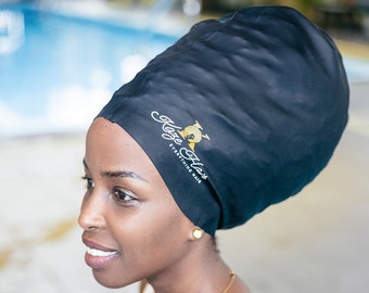 May include: A woman wearing a black satin shower cap with the text "Kase Elas" and "Everything Hair" on it. She is wearing a white tank top and a gold necklace.