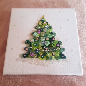 Peut inclure: Une toile blanche avec un sapin de No&euml;l en boutons verts d&eacute;cor&eacute; de boutons verts, roses et blancs, de strass et d'une &eacute;toile dor&eacute;e au sommet.