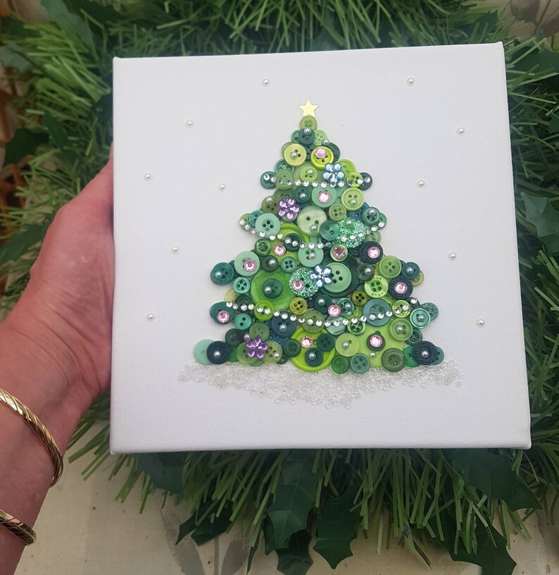 Peut inclure: Une toile blanche avec un sapin de No&euml;l en boutons verts. L'arbre est d&eacute;cor&eacute; de boutons verts, violets et blancs, ainsi que de strass argent&eacute;s et roses. L'arbre est entour&eacute; de paillettes blanches, qui ressemblent &agrave; de la neige.