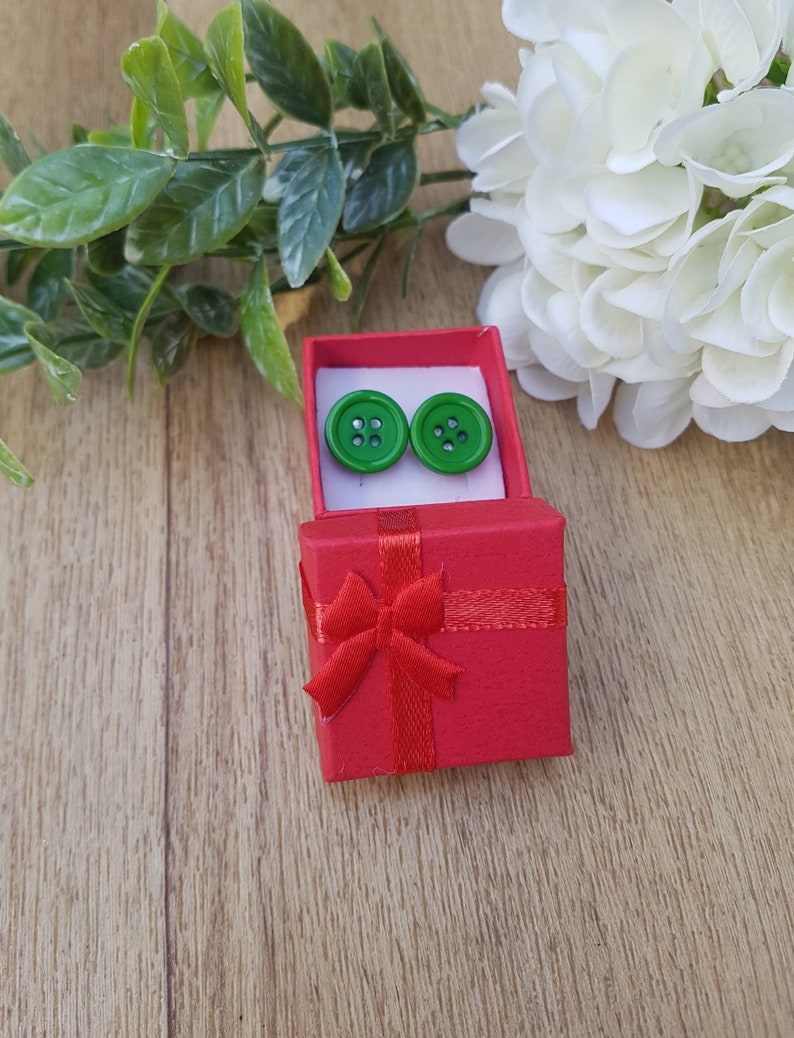 May include: A pair of green button earrings in a red gift box with a red ribbon bow.