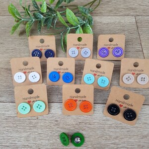 May include: Assortment of handmade button earrings on cards with the text "Handmade with Love". The earrings are in various colors, including blue, green, orange, white, and black.