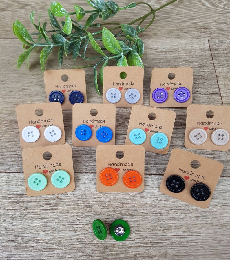 May include: Assortment of handmade button earrings on cards with the text "Handmade with Love". The earrings are in various colors, including blue, green, orange, white, and black.