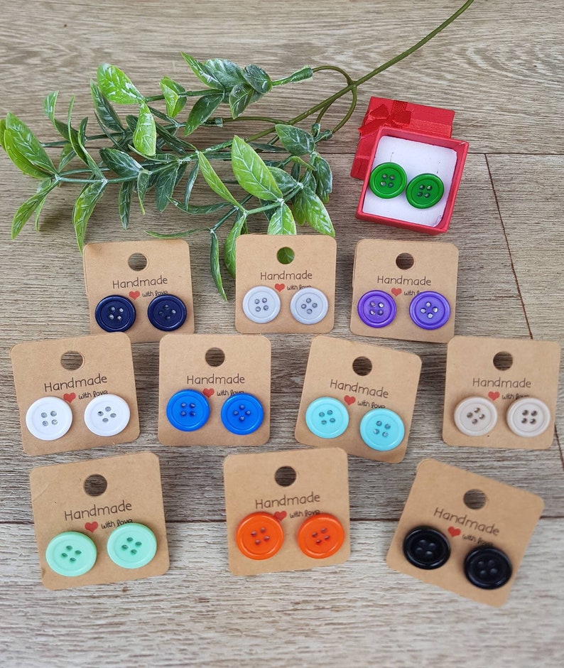 May include: Assortment of handmade button earrings displayed on cards with the text "Handmade with Love". The earrings are in various colors, including white, blue, green, orange, and black.