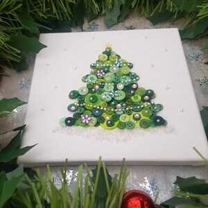 Peut inclure: Une toile blanche avec un sapin de No&euml;l en boutons verts d&eacute;cor&eacute; de boutons verts, roses et argent&eacute;s. L'arbre est entour&eacute; de paillettes blanches pour repr&eacute;senter la neige.