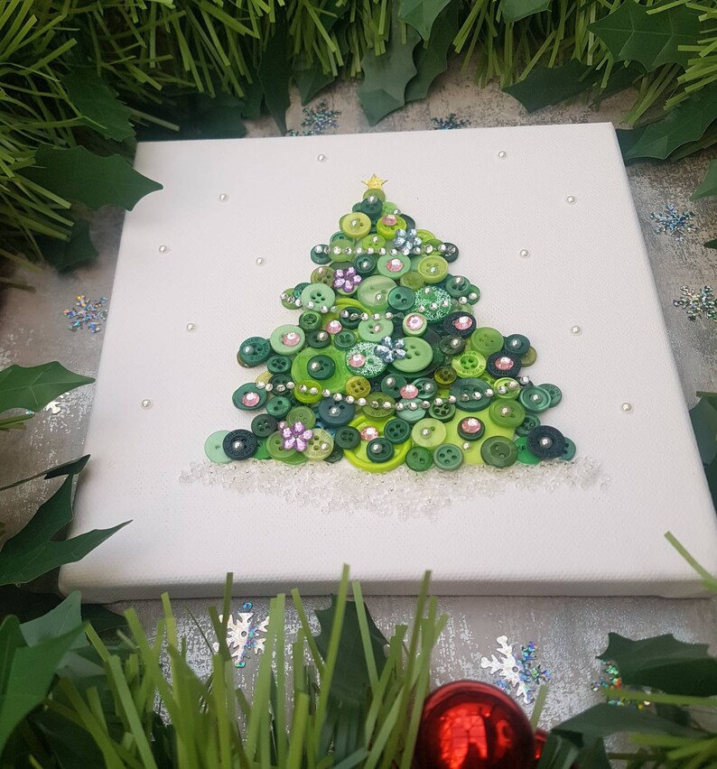 Peut inclure: Une toile blanche avec un sapin de No&euml;l en boutons verts d&eacute;cor&eacute; de boutons verts, roses et argent&eacute;s. L'arbre est entour&eacute; de paillettes blanches pour repr&eacute;senter la neige.
