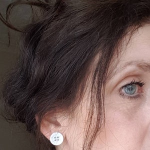 May include: A close-up of a person's ear with a small, round, white button earring. The earring has a four-hole design.