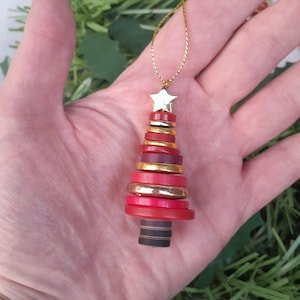 May include: A red and gold button Christmas tree ornament with a gold star on top. The ornament is hanging from a gold string.