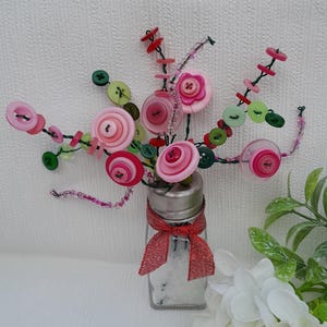 May include: A glass salt shaker with a red ribbon and a bouquet of pink, red, and green buttons arranged in a vase.