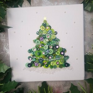 Peut inclure: Une toile blanche avec un sapin de No&euml;l en boutons verts. L'arbre est d&eacute;cor&eacute; de boutons verts, roses et bleus, ainsi que de paillettes et de strass. L'arbre est surmont&eacute; d'une &eacute;toile dor&eacute;e.