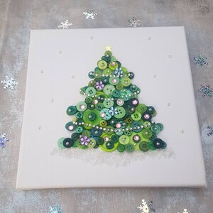 Peut inclure: Une toile blanche avec un sapin de No&euml;l en boutons verts. L'arbre est d&eacute;cor&eacute; de boutons verts, roses et argent&eacute;s. L'arbre est entour&eacute; de perles blanches.