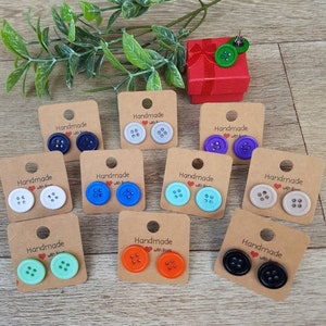 May include: Assortment of handmade button earrings in various colors, including black, white, blue, green, orange, and gray. Each pair is displayed on a small card with the text "Handmade with Love".