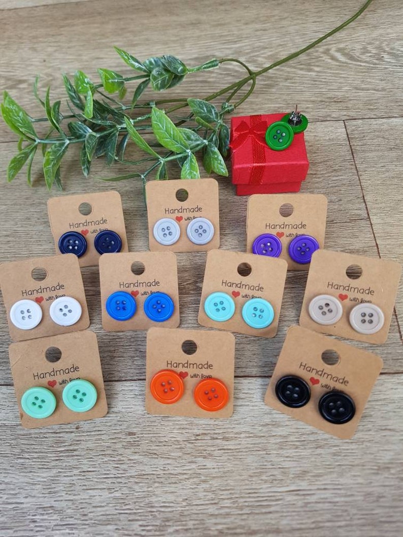 May include: Assortment of handmade button earrings in various colors, including black, white, blue, green, orange, and gray. Each pair is displayed on a small card with the text "Handmade with Love".