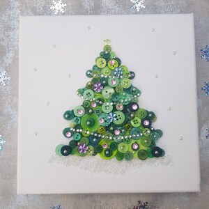 Peut inclure: Une toile blanche avec un sapin de No&euml;l en boutons verts d&eacute;cor&eacute; de boutons verts, roses et bleus, de strass et d'une &eacute;toile dor&eacute;e au sommet.