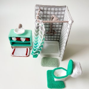 Peut inclure: Un ensemble de salle de bain en crochet avec une cabine de douche, des toilettes, un lavabo et des serviettes. La cabine de douche a un mur carrelé gris et blanc et un rideau de douche rayé vert et blanc. Les toilettes sont blanches avec un siège et un couvercle verts. Le lavabo est vert avec un bol blanc. Les serviettes sont rouges et blanches.