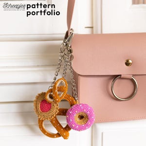 Puede incluir: Un bolso rosa con una cadena plateada y un llavero de alimentos de ganchillo. El llavero incluye un pretzel, una rosquilla y una galleta. El texto "Scheepjes pattern portfolio" está en la esquina superior izquierda.