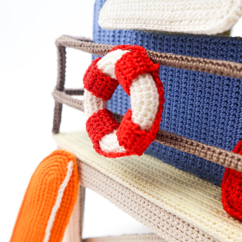 May include: Crocheted beach scene with a life preserver, a towel, and a lifeguard stand.