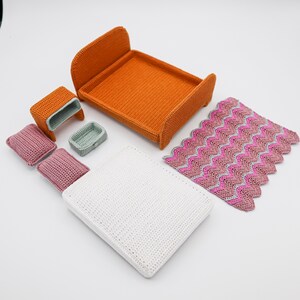 May include: A set of miniature crocheted furniture for a dollhouse, including a bed, nightstand, and a blanket. The bed is orange, the nightstand is brown, and the blanket is pink and white.