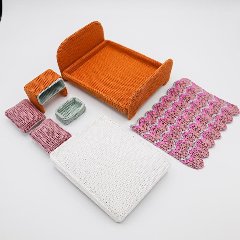 May include: A set of miniature crocheted furniture for a dollhouse, including a bed, nightstand, and a blanket. The bed is orange, the nightstand is brown, and the blanket is pink and white.
