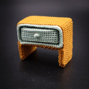 May include: A small crocheted nightstand with a drawer, made of brown and light blue yarn.